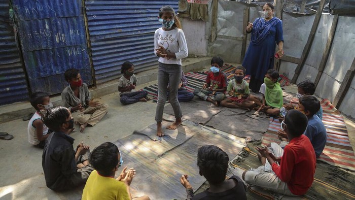 Kala Anak-anak Pemukiman Kumuh di India Ikut Kelas Online A teacher gestures as children wearing face masks as a precaution against the coronavirus attend online classes at a slum on the outskirts of Jammu, India, Monday, June 14, 2021. (AP Photo/Channi Anand)