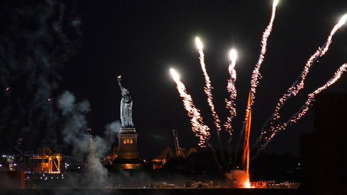 Pembatasan Dicabut, Warga New York Pesta Kembang Api Fireworks reflect off the water as they explode over New York Harbor and the Statue of Liberty as New York and other cities around New York state recognize a rate of 70% for single dose vaccinations against the COVID-19 virus, Tuesday, June 15, 2021 in New York. Celebration of the milestone was announced by Gov. Andrew Cuomo earlier in the day. (AP Photo/Craig Ruttle)