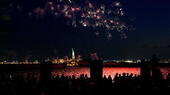 Pembatasan Dicabut, Warga New York Pesta Kembang Api Fireworks reflect off the water as they explode over New York Harbor and the Statue of Liberty as New York and other cities around New York state recognize a rate of 70% for single dose vaccinations against the COVID-19 virus, Tuesday, June 15, 2021 in New York. Celebration of the milestone was announced by Gov. Andrew Cuomo earlier in the day. (AP Photo/Craig Ruttle)