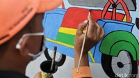Seorang petugas PPSU tengah menghias dinding di kawasan Halim Perdanakusuma dengan mural.