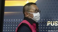 Adelin mengenakan masker dan kacamata. Tampangnya masih sedikit terlihat. Rambutnya cepak. Dia mengenakan rompi merah jambu Kejaksaan. 