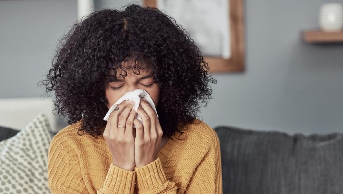 Shot of a young woman blowing her nose with a tissue at home