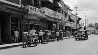 Penampakan aktivitas di salah satu ruas jalan Ibu Kota pada tahun 1963. Sebuah mobil tampak melintas di samping para pedagang yang mendorong gerobak untuk menjajakan beragam barang jualan mereka kepada sejumlah warga yang melintas.Keystone Features/Getty Images.    