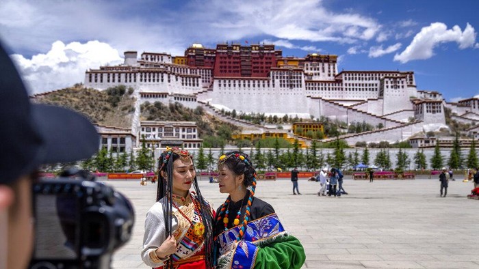 A Chinese tourist gets ready to pose for a photo atop a white yak being led by a Tibetan man in Namtso in western Chinas Tibet Autonomous Region, Wednesday, June 2, 2021. Tourism is booming in Tibet as more Chinese travel in-country because of the coronavirus pandemic, posing risks to the regions fragile environment and historic sites. (AP Photo/Mark Schiefelbein)
