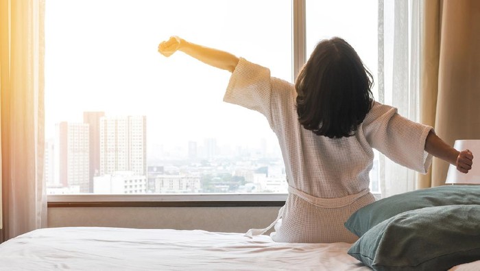Simple city lifestyle happy woman waking up in the morning taking some rest relaxing in luxury comfy city hotel room