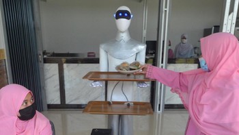 Dua robot berbentuk manusia dengan nampan di tangan yang berisi makanan mondar mandir di kafe untuk melayani makanan pesanan pengunjung. Robot itu sigap mengantarkan makanan dengan gerakan teratur dengan menggunakan sistem remote dan sensor yang mengikuti garis magnet.  