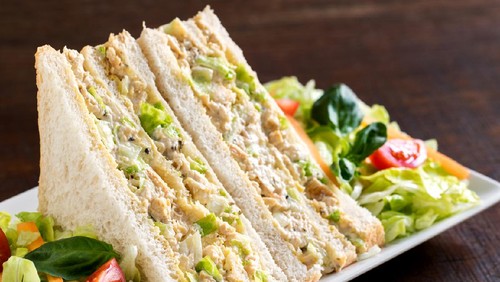 Macro close up white bread chicken and mayonnaise sandwich with green salad.