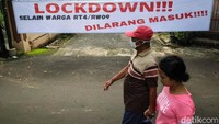 Warga melintas di depan spanduk lockdown atau karantina mikro di RT 4/9 di salah satu kelurahan di Kecamatan Pondok Karya, Tangerang Selatan, (23/6/2021).
