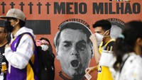 Pengunjuk rasa berjalan di depan mural bergambar Presiden Brazil, Jair Bolsonaro di São Paulo (19/6). Penanganan pandemi Corona menjadi isu politik yang panas di negeri samba itu. AP Photo/Marcelo Chello