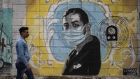Warga melintas di depan mural legenda musisi Tango, Carlos Gardel di Montevideo, Uruguay, (24/6). Tampak gambar Carlos Gardel menggunakan masker. AP Photo/Matilde Campodonico