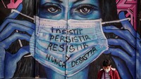 Warga berjalan di depan mural perempuan bermasker bertuliskan bersikeras, bertahan, melawan, dan pantang menyerah  di ibukota Bogota, Colombia (21/6).  Diego Cuevas/Getty Images