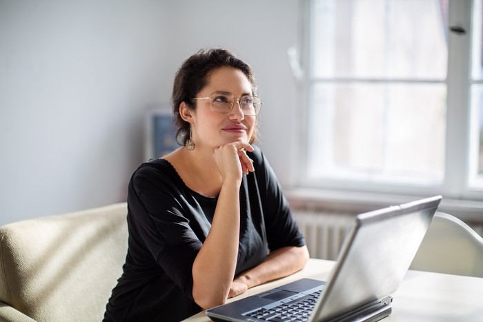 Businesswoman sitting in front of a laptop and thinking. Female is sitting at boardroom table with her laptop.