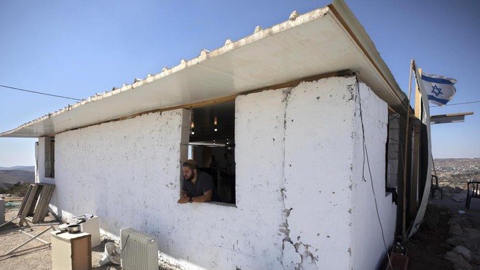An Israeli settler looks out of a window at the outpost of Eviatar near the northern West Bank town of Nablus, Monday, June 21, 2021. Settlers established the outpost last month and say it is now home to dozens of families. Palestinians say it is built on private land and fear it will grow and merge with other large settlements nearby. (AP Photo/Sebastian Scheiner)