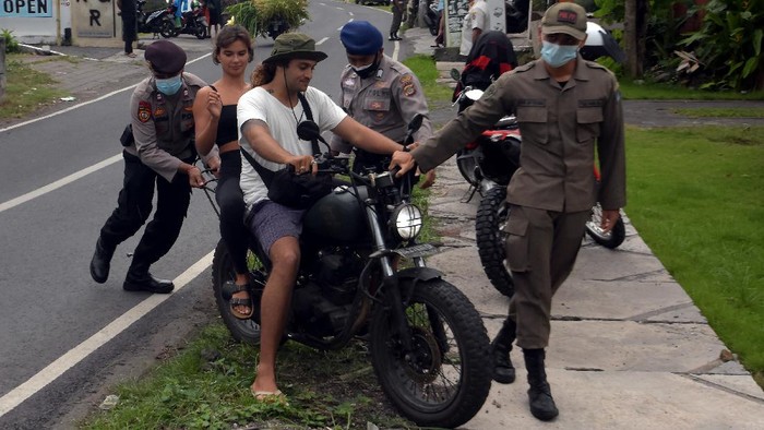 Anggota Polisi dan Satpol PP Kabupaten Badung menghentikan warga negara asing (WNA) yang melanggar protokol kesehatan saat operasi penertiban prokes dalam Pemberlakuan Pembatasan Kegiatan Masyarakat (PPKM) skala mikro di Desa Canggu, Badung, Bali, Jumat (25/6/2021). Tim satgas gabungan menindak sebanyak 18 orang WNA yang berasal dari berbagai negara tersebut untuk memberikan efek jera agar menerapkan protokol kesehatan dalam upaya pencegahan penyebaran varian baru COVID-19 di kawasan pariwisata itu. ANTARA FOTO/Nyoman Hendra Wibowo/aww.
