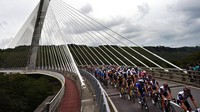 Rombongan pebalap saat melintasi jembatan pada etape pertama dari kota Brest dan berakhir di kota Landerneau (26/6/2021). AP/Daniel Cole