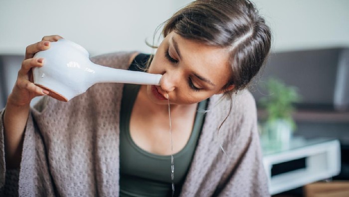 1240137425 One woman, young lady using neti pot at home.