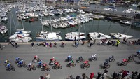 Para pebalap melintasi jalan di samping laut dengan jajaran kapal di etape kedua TDF 2021. Etape di pesisir barat Prancis ini dimulai di kota  Perros-Guirec dan berakhir di Mur-de-Bretagne Guerledan. AP Photo/Christophe Ena.