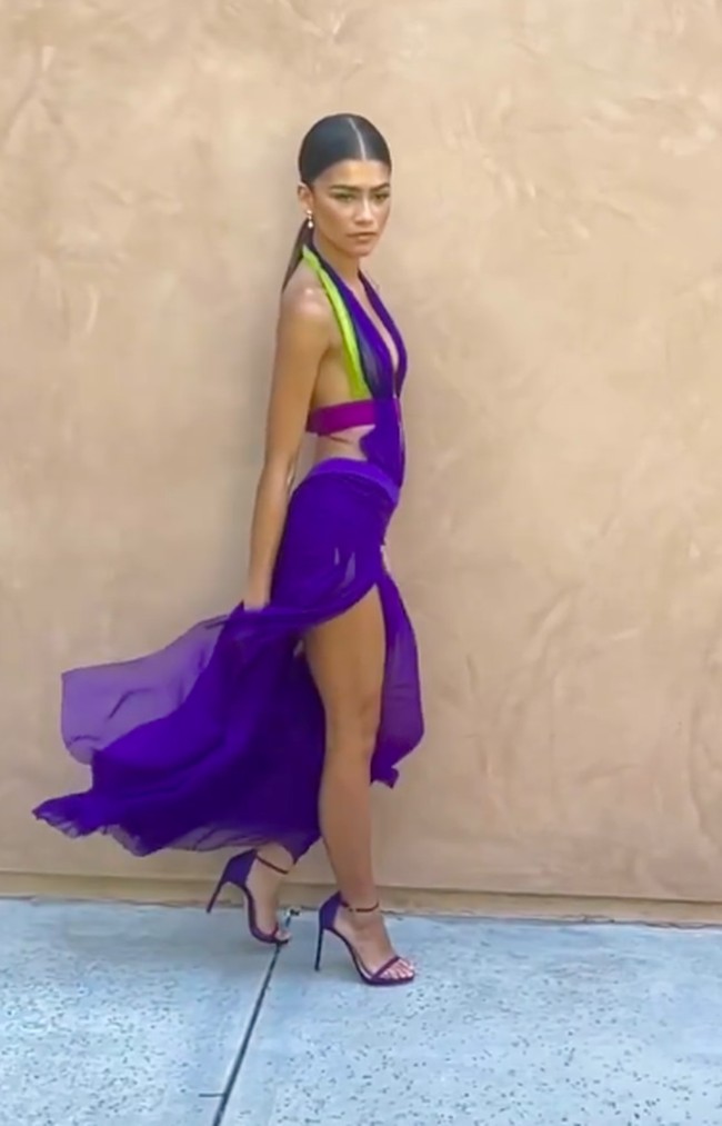 Aksen slim belt dan panel hijau pada halter-neck membuat penampilan serba ungu ini jauh dari kesan monoton. Bahan chiffon yang tipis cenderung transparan memberi efek juntaian yang elegan ketika Zendaya melangkah. Kaki jenjangnya yang ditopang sandal-heels senada pun terekspos berkat belahan tinggi rok gaunnya. (Foto: Instagram/@zendaya)