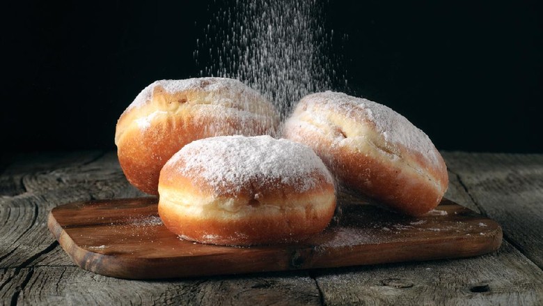 Three donut sprinkled with powdered sugar on wooden table on black background closeup. Food background