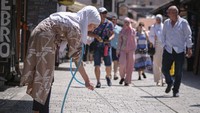 Seorang penjaga toko menyemprotkan air untuk mendinginkan trotoar pada hari yang panas di Sarajevo, Bosnia, (23/6/2021). AP Photo/Kemal Softic.