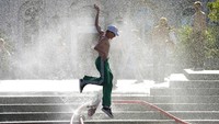 Seorang remaja bermain air yang sengaja disemprotkan untuk mendinginkan taman kota di  Warsawa, Polandia, (21/6/2021). Temperatur sejumlah daerah di Polandia dilaporkan hingga 35 derajat Celcius. AP Photo/Czarek Sokolowski.