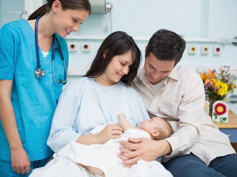 Father and mother holding a new born baby with a doctor in a hospital room