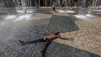 Seorang pria sampai berbaring agar suhu badannya dingin di pancuran air. Foto: AP