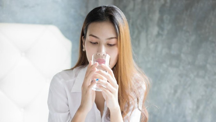 Asian Young woman drinking glass of water in bed at morning