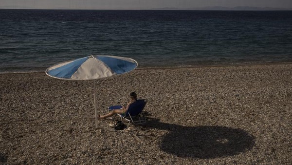 Seorang turis duduk di tepi pantai Aegean, Samos Yunani. Sepi, Yunani merindukan kehadiran banyak turis di tengah pandemi (AP)