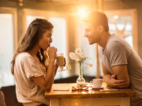 Young woman drinking coffee and communicating with her smiling boyfriend in a cafe.