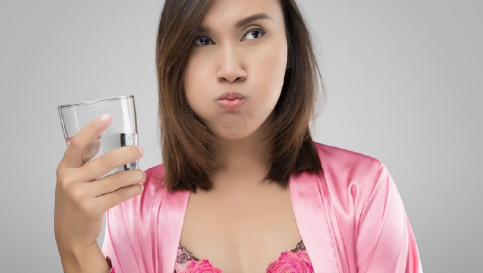 814415918 kumur Woman rinsing and gargling while using mouthwash from a glass, During daily oral hygiene routine, Girl in a pink silk nightwear, Dental Healthcare Concepts