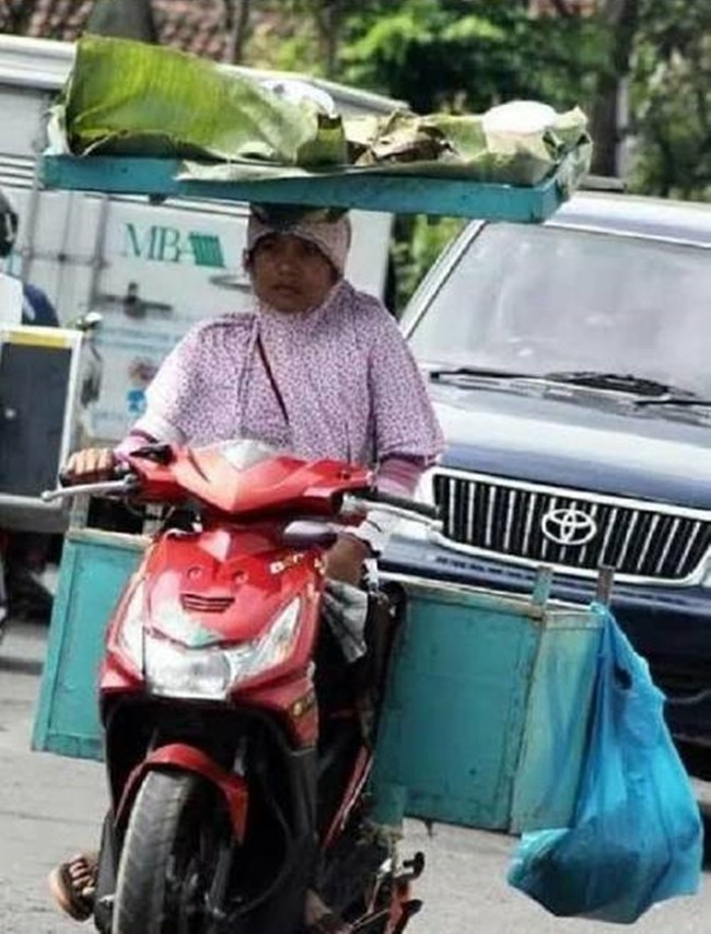 Dari foto ini terbukti bahwa emak-emak memang jago banget multitasking. Lihat saja emak yang satu ini, bisa naik motor sambil bawa barang di kepalanya. Foto: 1cak.com