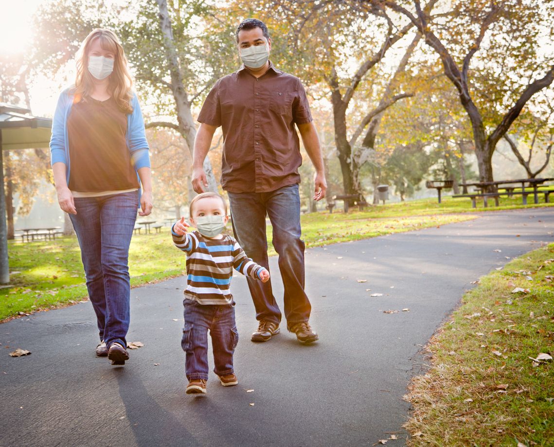 A happy family wear face masks while walking in their neighborhood during the COVID-19 pandemic.
