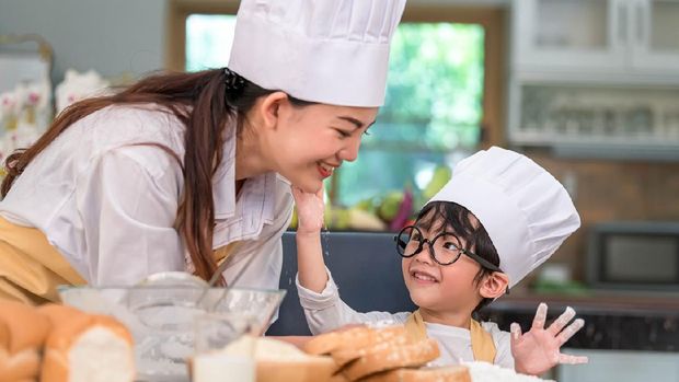 Cute little Asian boy painting beautiful woman face with dough flour. Chef team playing and baking bakery in kitchen funny. Homemade food and bread. Education and people lifestyles learning concept