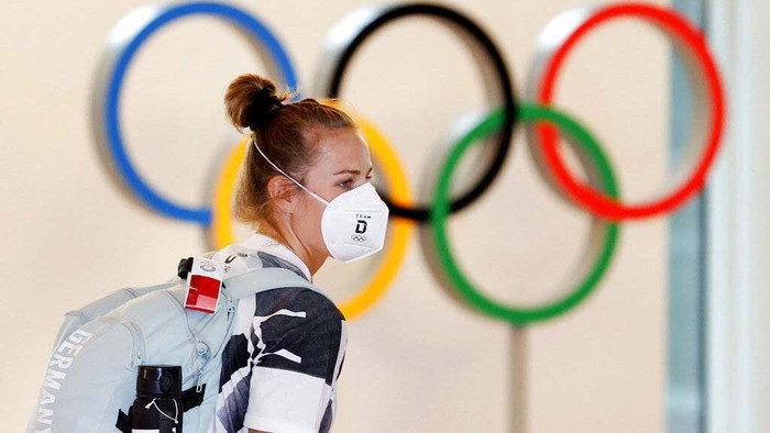 A German athlete, wearing face mask, walks past the Olympic rings display on their arrival at Haneda airport in Tokyo, Thursday, July 1, 2021. The pressure of hosting an Olympics during a still-active pandemic is beginning to show in Japan. The games begin July 23, with organizers determined they will go on, even with a reduced number of spectators or possibly none at all.(Kyodo News via AP)