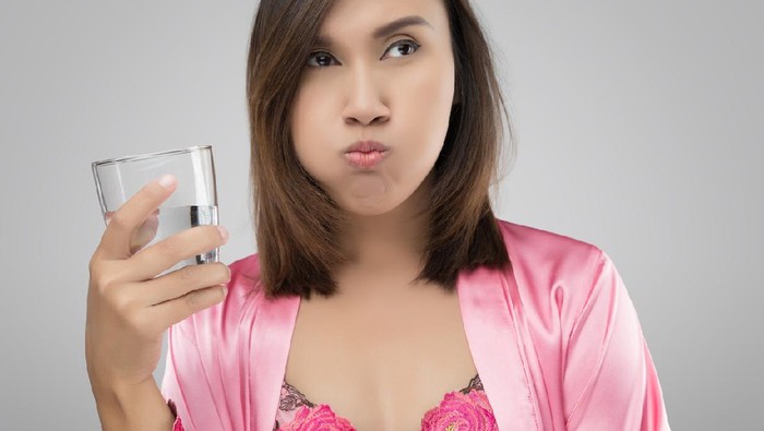 814415918 Woman rinsing and gargling while using mouthwash from a glass, During daily oral hygiene routine, Girl in a pink silk nightwear, Dental Healthcare Concepts