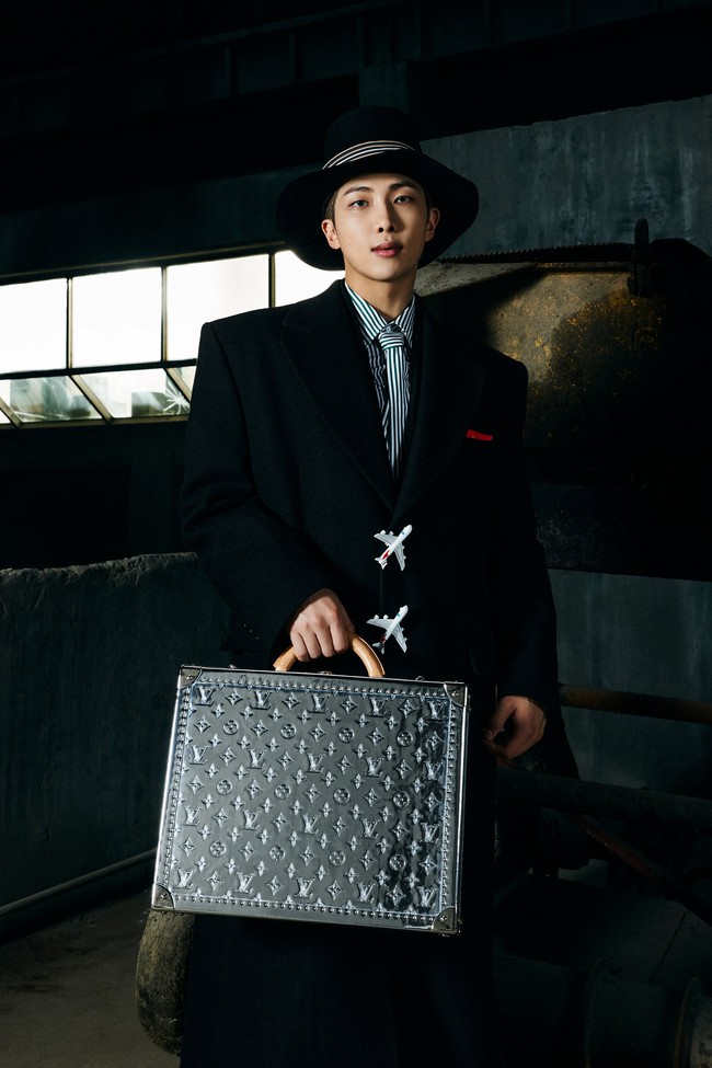Jimin kemudian menoleh ke arah RM BTS, yang berjalanan menuruni anak tangga. Leader grup BTS itu tampil mengenakan coat panjang berwarna hitam sambil menjinjing tas silver Valise Cotteville 40 dengan logo Louis Vuitton. Foto: dok. Louis Vuitton