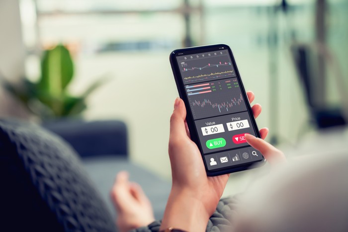 Stock exchange market concept, businesswoman trader looking on smartphone with graphs analysis candle line on sofa in house, diagrams on screen.