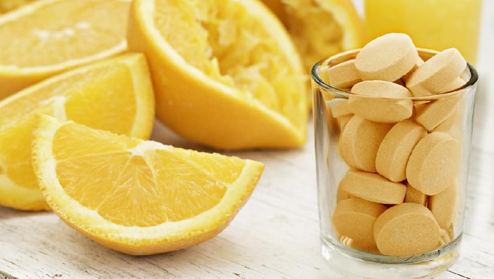 Ilustrasi Vitamin C A close up shot of sliced and squeezed oranges a glass of orange juice and a glass full of orange flavored vitamin C Pills. Eat the orange, drink the juice or take a pill.
