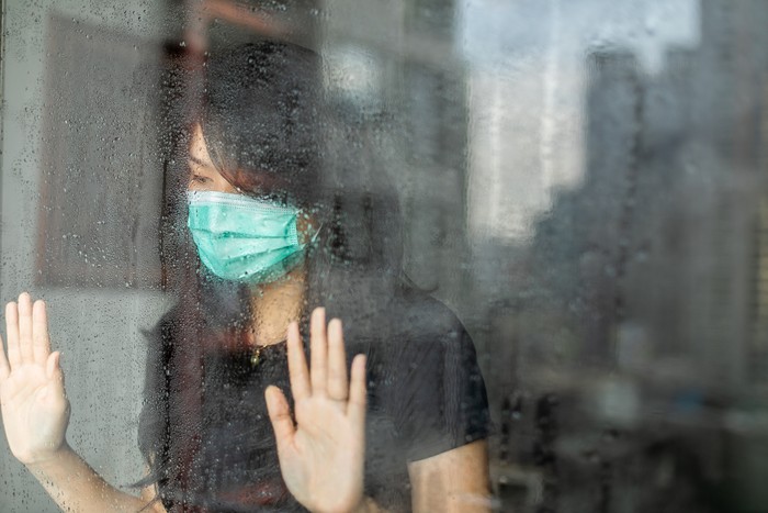 Young woman in isolation at home for coronavirus  looking out of window during rain