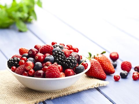 White bowl filled with fresh mixed organic berries on blue garden table. Some berries are scattered outside the bowl. DSRL studio photo taken with Canon EOS 5D Mk II and Canon EF 100mm f/2.8L Macro IS USM
