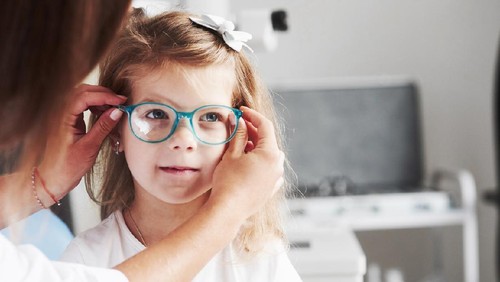 New look. Doctor giving the child new glasses for her vision.