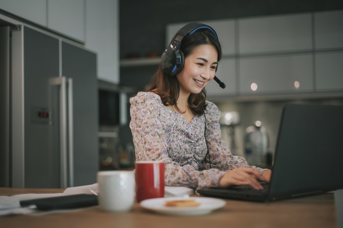 an asian chinese beautiful woman working from home as customer service answering to her customer online using laptop and headphone in the kitchen typing