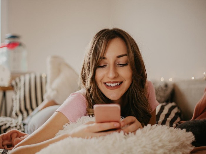 1126400321 Happy young woman caller talking on the phone at home, cheerful teen girl enjoys pleasant mobile conversation, smiling millennial female holding cell speaking making call by telephone in living room