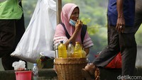 Pedagang jamu menunggu pembeli dengan duduk di atas trotoar di kawasan Bekasi.