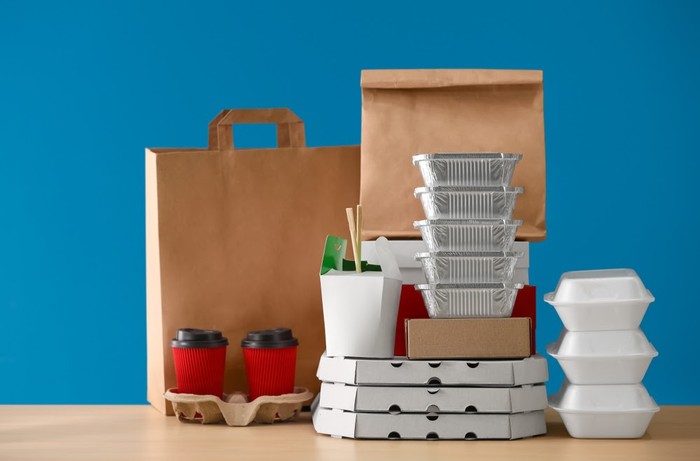 Different packages and carton cups on table against color background. Food delivery service Different packages and carton cups on table against color background. Food delivery service