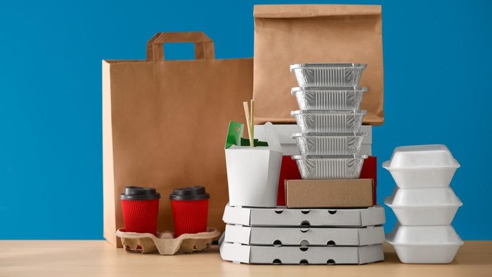 Different packages and carton cups on table against color background. Food delivery service