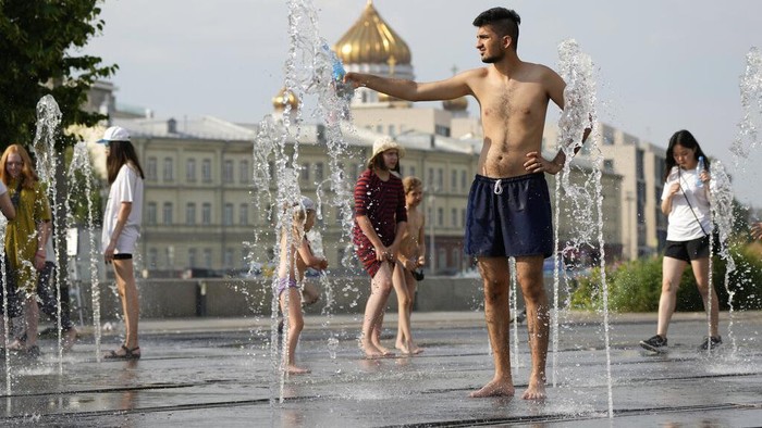 A couple share a moment as children play in a fountain at a park next to an embankment of the Moscow River in Moscow, Russia, Wednesday, July 14, 2021. The hot weather in Moscow is continuing with temperatures reach 34 degrees Celsius during a day. (93,2 Fahrenheit). (AP Photo/Pavel Golovkin)