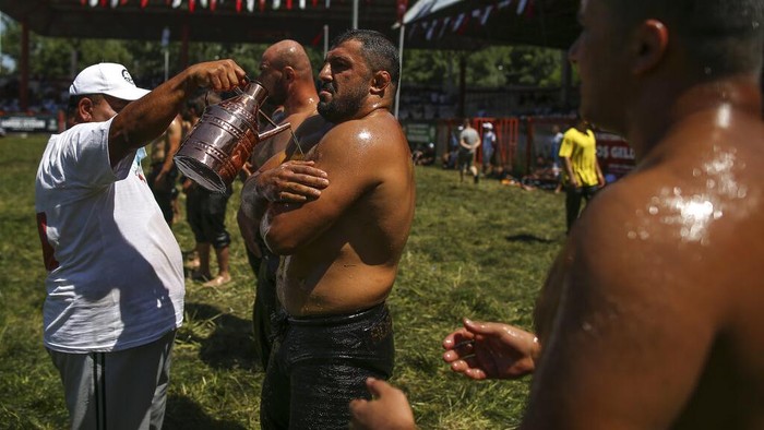 An 'oiler', someone charged with oiling up wrestlers and filling up oil pitchers, douses wrestlers in olive oil, during the 660th instalment of the annual Historic Kirkpinar Oil Wrestling championship, in Edirne, northwestern Turkey, Saturday, July 10, 2021.Thousands of Turkish wrestling fans flocked to the country's Greek border province to watch the championship of the sport that dates to the 14th century, after last year's contest was cancelled due to the coronavirus pandemic. The festival, one of the world's oldest wrestling events, was listed as an intangible cultural heritage event by UNESCO in 2010. (AP Photo/Emrah Gurel)