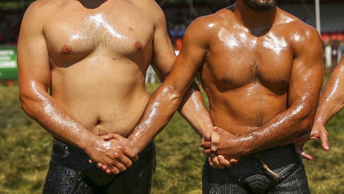 Serunya Kontes Gulat Minyak di Turki An 'oiler', someone charged with oiling up wrestlers and filling up oil pitchers, douses wrestlers in olive oil, during the 660th instalment of the annual Historic Kirkpinar Oil Wrestling championship, in Edirne, northwestern Turkey, Saturday, July 10, 2021.Thousands of Turkish wrestling fans flocked to the country's Greek border province to watch the championship of the sport that dates to the 14th century, after last year's contest was cancelled due to the coronavirus pandemic. The festival, one of the world's oldest wrestling events, was listed as an intangible cultural heritage event by UNESCO in 2010. (AP Photo/Emrah Gurel)